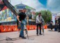 Two men operating jackhammers on a paved plaza at an outdoor event, with orange barriers and sponsor banners in the background, including TAMEX signage.