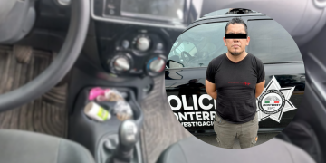Suspect standing in front of a police vehicle with a star badge visible on the side; eyes covered with a black bar and wearing a black t‑shirt.