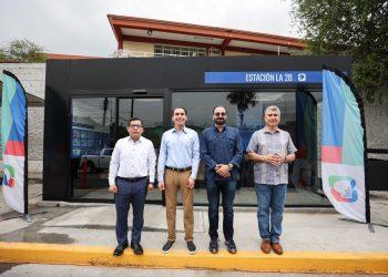Four men stand in a line outside a glass-front building with a blue Estación La 28 sign and colorful banners on either side.