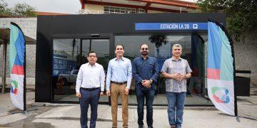 Four men stand in a line outside a glass-front building with a blue Estación La 28 sign and colorful banners on either side.