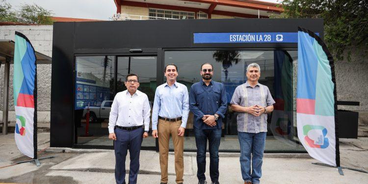 Four men stand in a line outside a glass-front building with a blue Estación La 28 sign and colorful banners on either side.