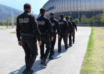 Monterrey police officers walking in formation along a walkway beside a large stadium.