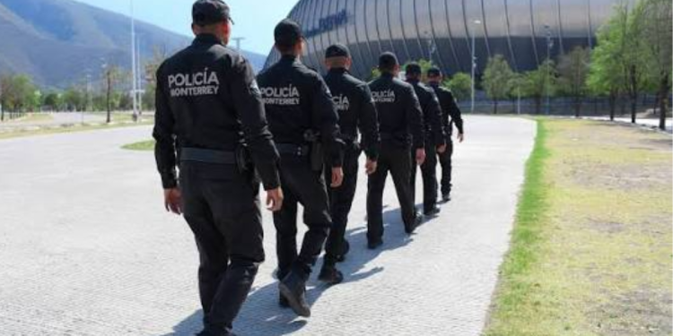 Monterrey police officers walking in formation along a walkway beside a large stadium.